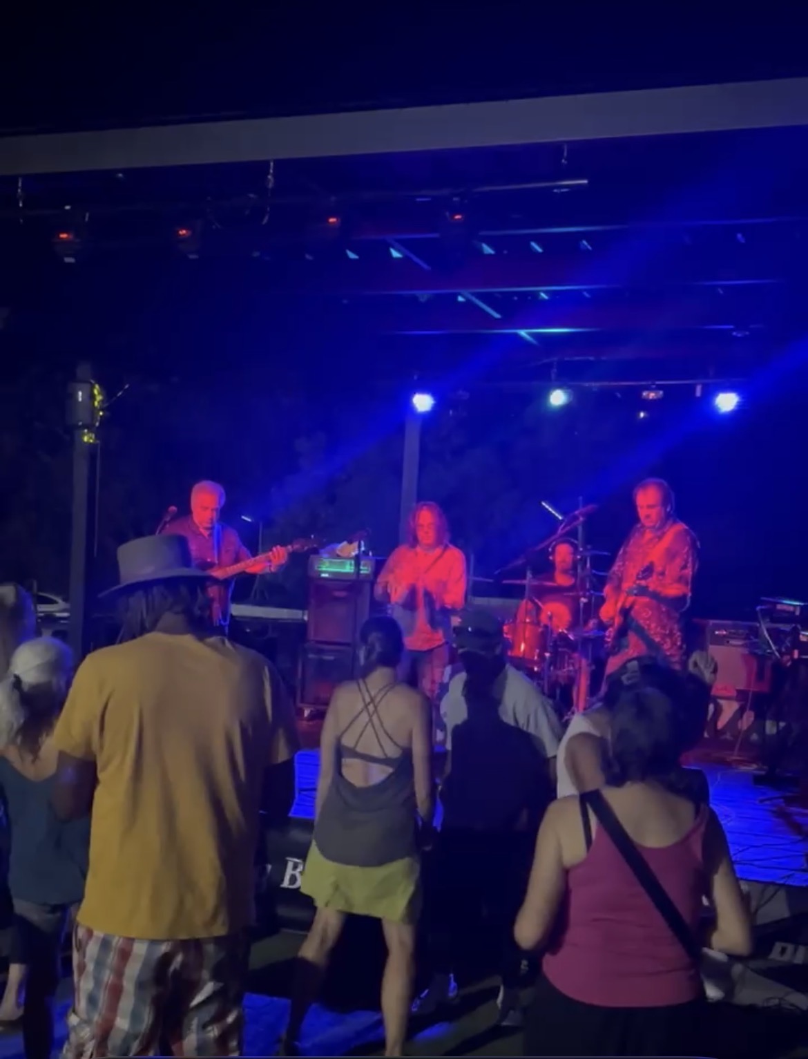 Band rocking out under vibrant blue and violet stage lights with dancers